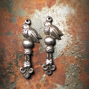 May include: Two silver bird charms with a beaded design and a three-pronged base.