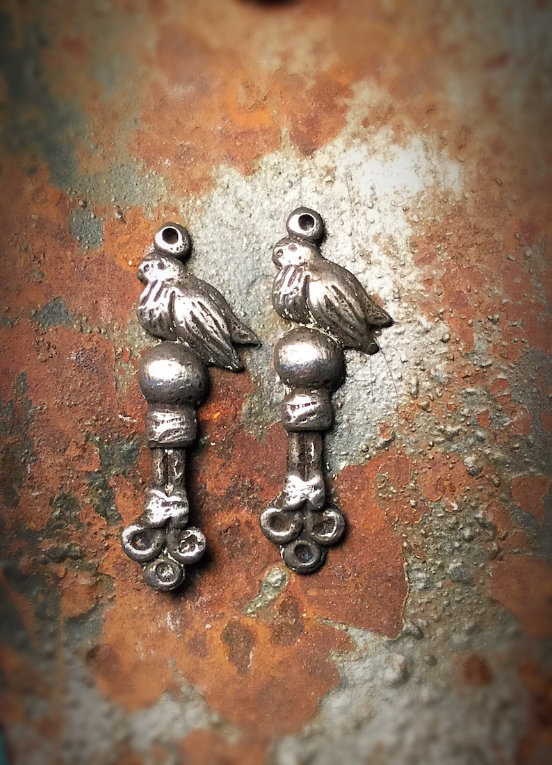 May include: Two silver bird charms with a beaded design and a three-pronged base.