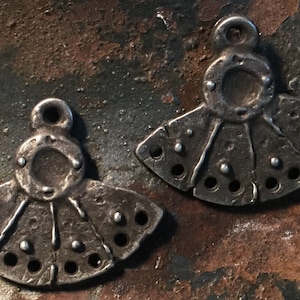 May include: Two silver-toned metal charms in the shape of a fan with a circle in the center. The charms have a textured surface and a loop at the top for hanging.