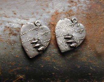 May include: Two silver heart-shaped pendants with a textured finish. Each pendant has the words "live simply, keep today, I you" inscribed. The pendants have a small loop at the top for hanging.
