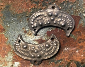 May include: Two silver-colored metal crescent-shaped decorative pieces with a textured surface. The pieces have a raised, beaded design around the edges and a series of raised dots in the center.