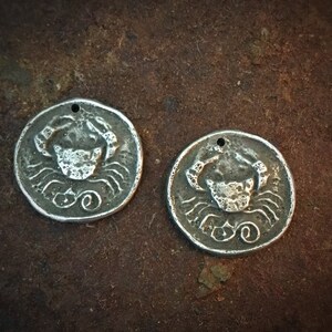 Peut inclure: Deux breloques en métal argenté avec un motif de crabe. Les breloques sont rondes et ont un trou en haut pour les suspendre.