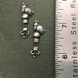May include: Two silver-toned metal charms shaped like birds with a small ball and a decorative design at the bottom. The charms are about 1 inch long and are shown next to a ruler.