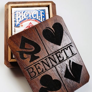 May include: A wooden box with a hinged lid, the lid is open and reveals a deck of Bicycle playing cards. The box is decorated with a black heart, spade, club, and the name "BENNETT".