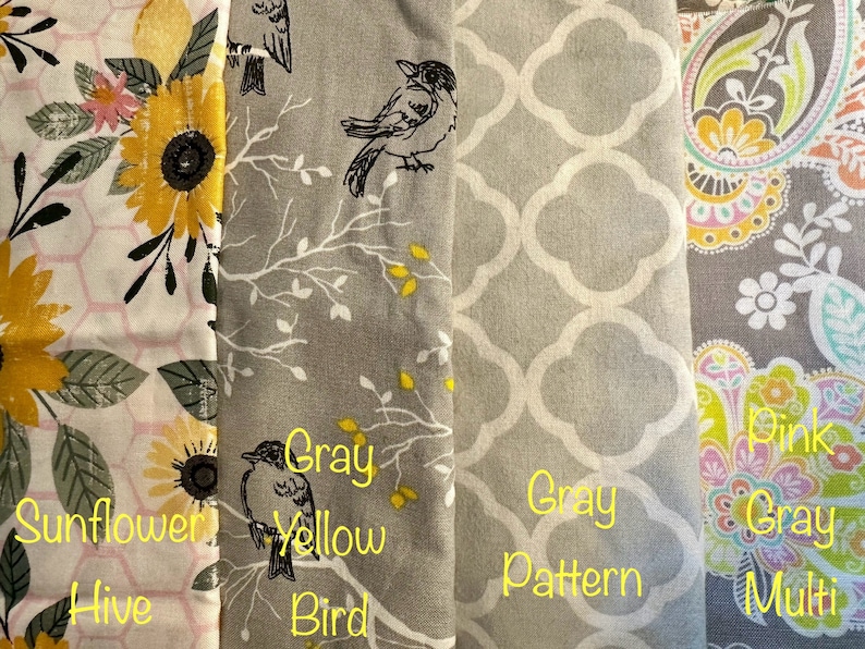 May include: Four fabric swatches with different patterns and colors. The first swatch is a white background with a pink and yellow sunflower pattern and the text "Sunflower Hive". The second swatch is a gray background with a black bird and branches and the text "Gray Yellow Bird". The third swatch is a gray background with a white geometric pattern and the text "Gray Pattern". The fourth swatch is a gray background with a pink, yellow, and green floral pattern and the text "Pink Gray Multi".