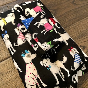 May include: Black fabric wallet with a repeating pattern of white dogs wearing colorful accessories. The dogs are wearing bows, collars, and bandanas.