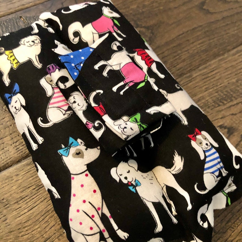 May include: Black fabric wallet with a repeating pattern of white dogs wearing colorful accessories. The dogs are wearing bows, collars, and bandanas.