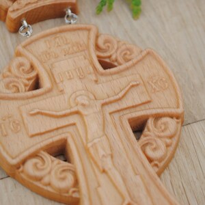 May include: A wooden cross with intricate carvings and a depiction of Jesus Christ. The cross is made of light brown wood and has a traditional design.