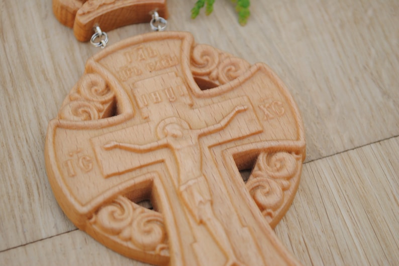 May include: A wooden cross with intricate carvings and a depiction of Jesus Christ. The cross is made of light brown wood and has a traditional design.