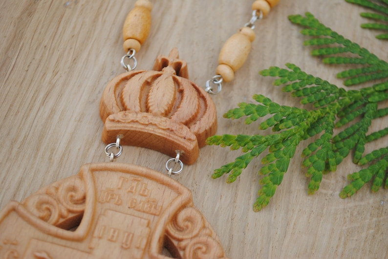 May include: A wooden pendant necklace featuring a carved crown and cross. The cross has the words "I AM THE WAY" inscribed on it. The necklace is made from wooden beads and silver chains.