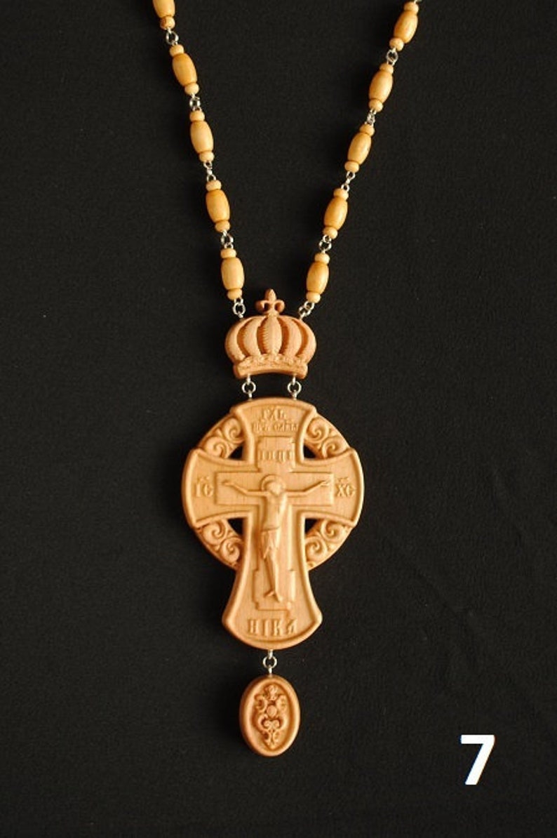 May include: A wooden cross necklace featuring a crown, a figure of Jesus Christ, and a small pendant. The cross is intricately carved with details and the words "IC XC NIKA" are visible.