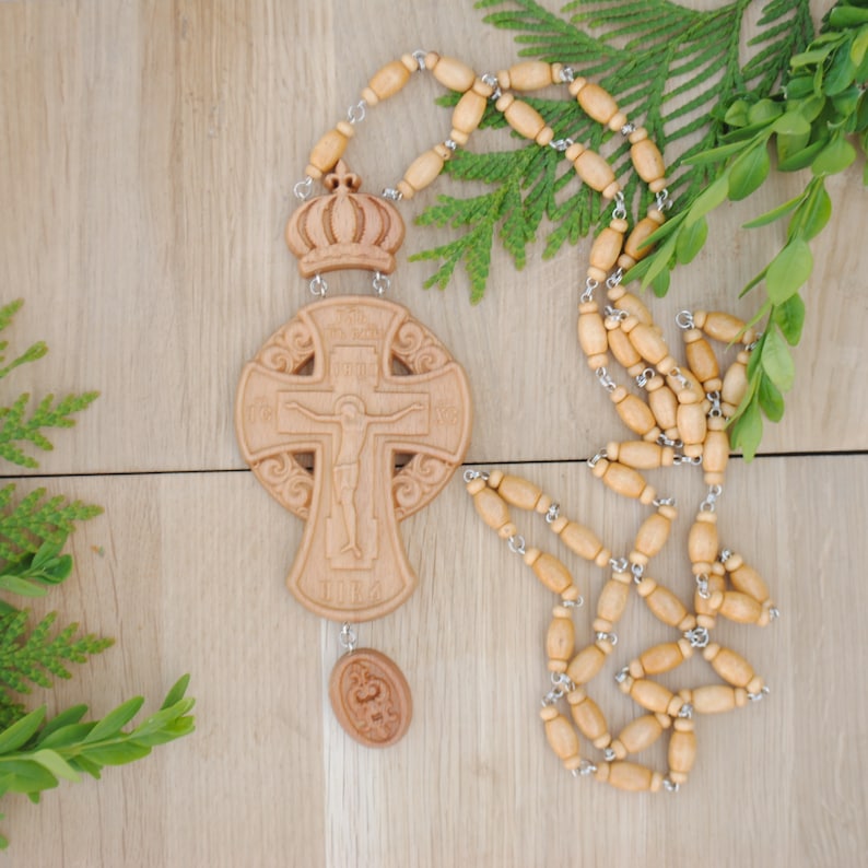 May include: A wooden cross with a carved image of Jesus Christ on the front. The cross is attached to a wooden rosary with a crown at the top. The rosary is made of light brown wood beads and silver metal.