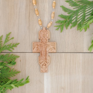 May include: A wooden cross with intricate carvings depicting a religious scene. The cross is attached to a beaded chain.
