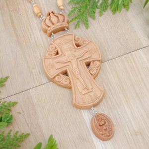 May include: A wooden cross with intricate carvings and a small crown pendant. The cross features a figure of Jesus Christ on the front and Cyrillic text around the edges.