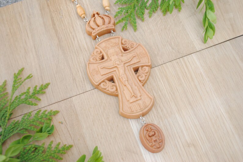 May include: A wooden cross with intricate carvings and a small crown pendant. The cross features a figure of Jesus Christ on the front and Cyrillic text around the edges.