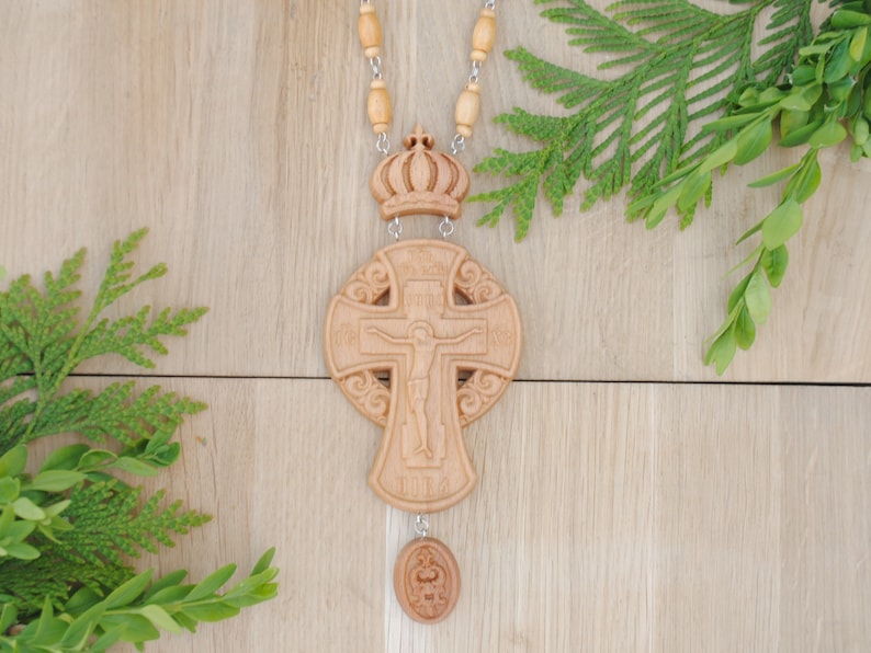 May include: A wooden cross with a carved image of Jesus Christ on the front. The cross is on a beaded chain with a crown at the top and a small round pendant at the bottom.