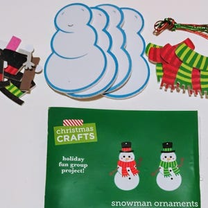 May include: A Christmas crafts kit with snowman ornaments. The kit includes snowman cutouts, hats, scarves, and pipe cleaners. The package reads "Holiday fun group project!" and features two snowman illustrations.