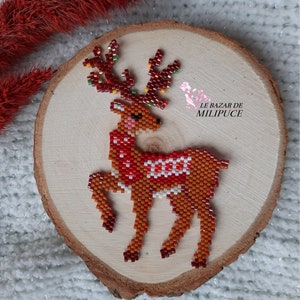 May include: A beaded reindeer ornament with a red and white scarf, brown body, and gold antlers. The ornament is displayed on a wooden slice.