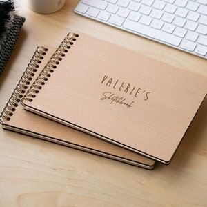 May include: Two wooden spiral bound sketchbooks with a natural wood finish. The top sketchbook has the text "VALERIE'S Sketchbook" engraved on the cover.