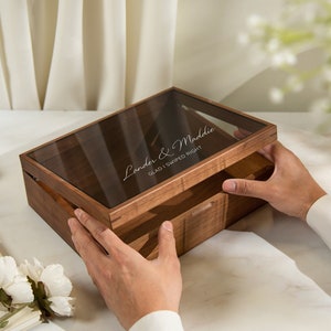 May include: A wooden box with a glass lid, engraved with the text "Lander & Maddie Glad I Swiped Right". The box is open and the lid is being lifted by a hand.