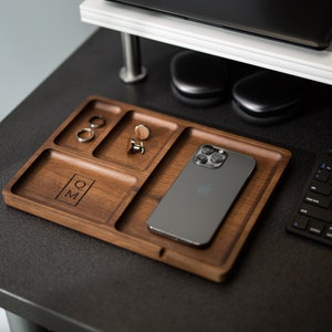 May include: A wooden tray with four compartments, one for a phone, one for rings, one for cufflinks, and one with the initials "Q.M." engraved.