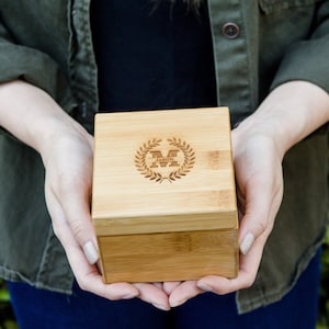 May include: A wooden box with a lid, engraved with a laurel wreath and the initials "M" and the name "Jason".