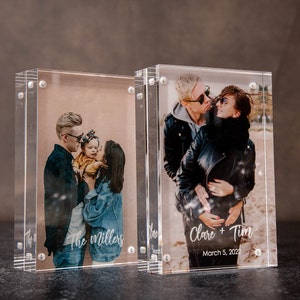 May include: Two clear acrylic photo blocks displaying family photos. One block features a family with the text "The Millers". The other block shows a couple with the text "Clare + Tim" and the date "March 5, 2022".