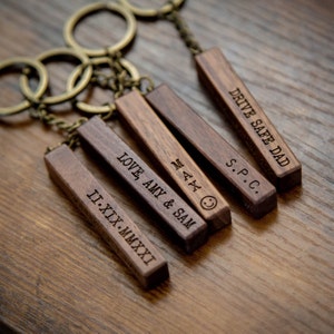 Peut inclure: Cinq porte-clés en bois avec des messages gravés. Les porte-clés sont attachés à un ensemble de porte-clés en métal. Les messages sur les porte-clés sont "DRIVE SAFE DAD", "S.P.C.", "MAX", "LOVE, AMY & SAM", et "II-XIX-MMXXI".
