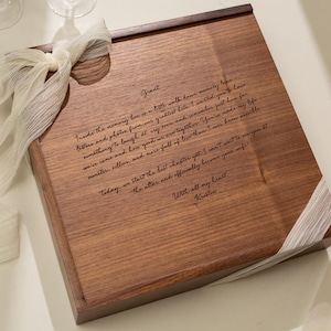 May include: A square wooden memory box with a dark brown finish, featuring a laser-engraved handwritten letter on the lid. The text begins with Grant and ends with With all my heart, Kristin. A cream-colored crinkled ribbon is tied around the box.