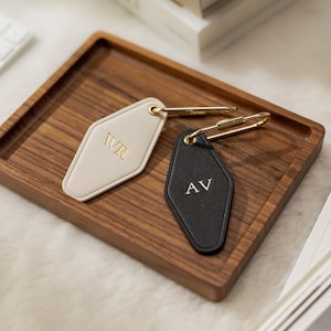 May include: Two diamond-shaped hotel-style key tags with gold-tone metal hardware. One tag is cream-colored with the gold embossed letters WR, and the other is black with the silver embossed letters AV. Both tags feature a gold-tone metal carabiner.