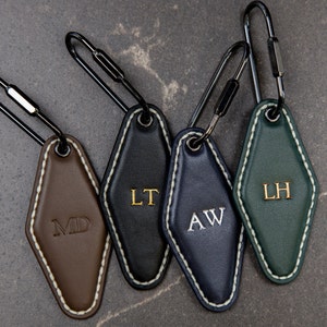 May include: Four leather keychains with different coloured leather and gold lettering. The keychains are in the shape of a diamond and have the initials "MD", "LT", "AW", and "LH" on them.