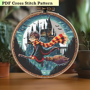 Puede incluir: Un patrón de punto de cruz con Harry Potter volando en una escoba frente al castillo de Hogwarts. El patrón está en un aro circular e incluye una luna llena, murciélagos y un cielo azul oscuro.