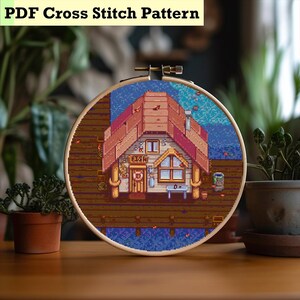 May include: A cross-stitch design in a wooden hoop, depicting a pixelated house on a pier. The house has a red roof and a sign that reads "FISH". The text "PDF Cross Stitch Pattern" is displayed at the top of the image.