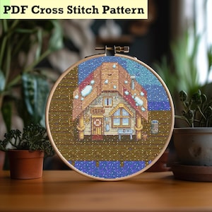 May include: A cross-stitch design in a wooden hoop shows a pixelated house with snow on the roof and a blue sky. The text "PDF Cross Stitch Pattern" is at the top. The house has a door, windows, and a chimney.