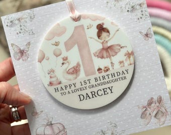 Puede incluir: Una tarjeta redonda rosa y blanca con una ilustración de bailarina y el número uno. La tarjeta dice "Feliz 1er cumpleaños a una adorable nieta Darcey".
