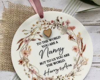 Könnte beinhalten: Runder weißer Keramik-Anhänger mit Blumenmuster und dem Text "To the world you are a Nanny but to us you are the world. Harry & Ava".