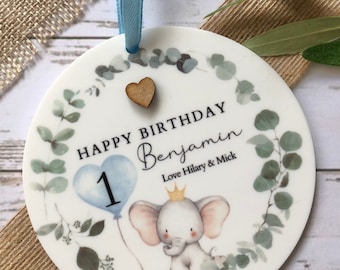May include: A white round ornament with a blue and white balloon, a cute elephant with a crown, and the text "Happy Birthday Benjamin Love Hilary & Mick".