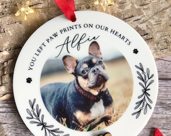 May include: White ceramic Christmas ornament with a photo of a black and tan French Bulldog. The ornament has the text "You left paw prints on our hearts Alfie" and a small wooden heart.