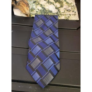May include: A blue necktie with a geometric pattern of squares and rectangles in shades of blue, black, and gray. The tie is made of a smooth fabric and has a classic pointed end. A stylish accessory for formal or business attire.