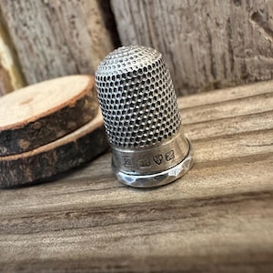 Puede incluir: Un dedal de plata con una superficie texturizada y marcas de contraste en la parte inferior.