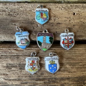 Puede incluir: Seis colgantes de plata vintage con detalles de esmalte. Cada colgante tiene forma de escudo y presenta un estado o ciudad australiano diferente. Los colgantes incluyen: Australia, Nobby's Newcastle, Newcastle, Melbourne, Tasmania y Victoria.