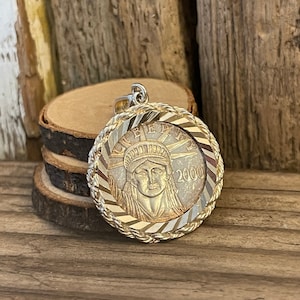 May include: A silver and gold pendant featuring a 2000 Liberty coin with a rope-like border. The coin depicts the Statue of Liberty with the word "LIBERTY" inscribed around the edge.