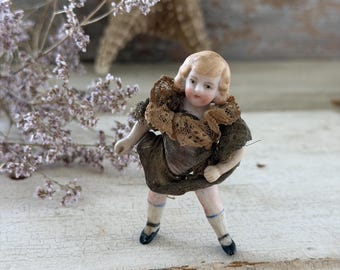 Puede incluir: Una pequeña figura de porcelana de un niño con cabello rubio, vestido con un traje marrón oscuro con cuello de encaje con volantes, calcetines blancos con rayas azules y zapatos negros, en una pose dinámica con los brazos extendidos.