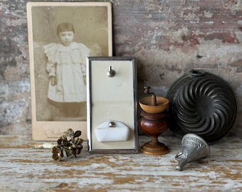 Puede incluir: Naturaleza muerta de objetos antiguos. Incluye una foto de un niño, un broche floral de latón, un jabonera de pared enmarcada, un molinillo de café de madera, un embudo de metal y un molde decorativo para pasteles.