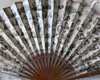 Puede incluir: Abanico de mano antiguo con mango de madera marrón y abanico de papel con retratos en blanco y negro. Los bordes del abanico están adornados con detalles en rosa y dorado. El abanico está abierto, mostrando numerosas figuras históricas.