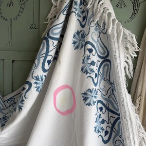 Puede incluir: Textil blanco con un estampado floral azul y ribete de flecos. El dise&ntilde;o presenta flores estilizadas y formas tipo paisley. El textil tiene una mancha marcada con un c&iacute;rculo rosa.