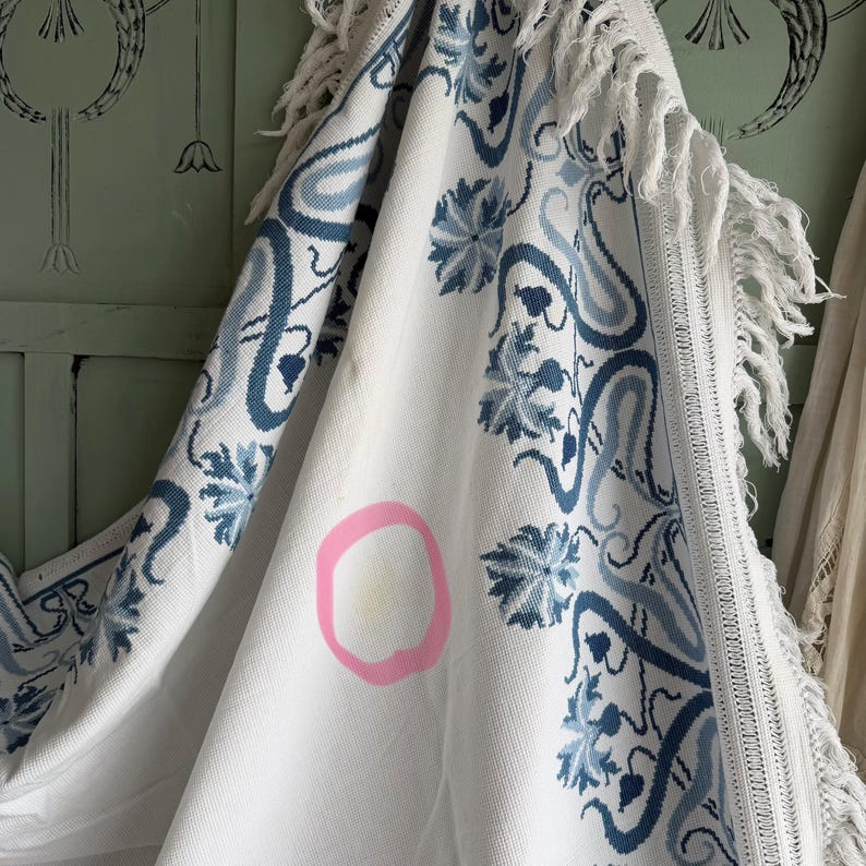 Puede incluir: Textil blanco con un estampado floral azul y ribete de flecos. El dise&ntilde;o presenta flores estilizadas y formas tipo paisley. El textil tiene una mancha marcada con un c&iacute;rculo rosa.