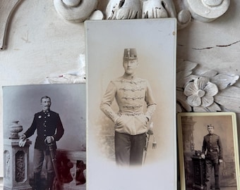 Puede incluir: Colección de fotografías antiguas que muestran a hombres uniformados. La imagen central es un retrato de un hombre con uniforme militar claro con una chaqueta decorativa y un sombrero. Otras fotos muestran a hombres con uniformes oscuros, uno con una espada.