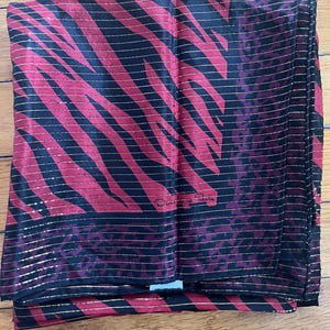 May include: A folded scarf with a bold zebra stripe pattern in red and black, accented with thin gold stripes. The scarf has a label that reads "Oscar de la Renta".