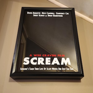 May include: A black framed movie poster with the title "SCREAM" in white letters with a red outline. The poster is for the Wes Craven film starring David Arquette, Neve Campbell, Courteney Cox, Skeet Ulrich, and Drew Barrymore. The tagline is "Someone's taken their love of scary movies one step too far!"